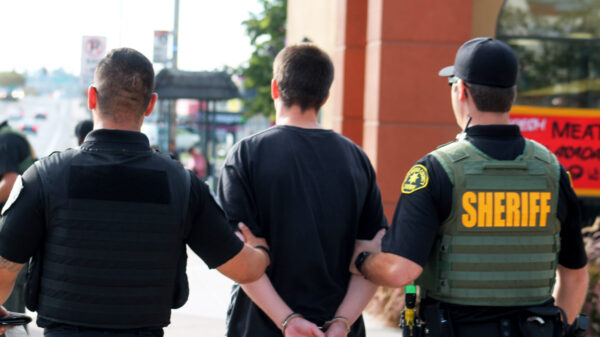 A male in handcuffs is being escorted away by a San Diego Police Department officer and a San Diego County Sherrif