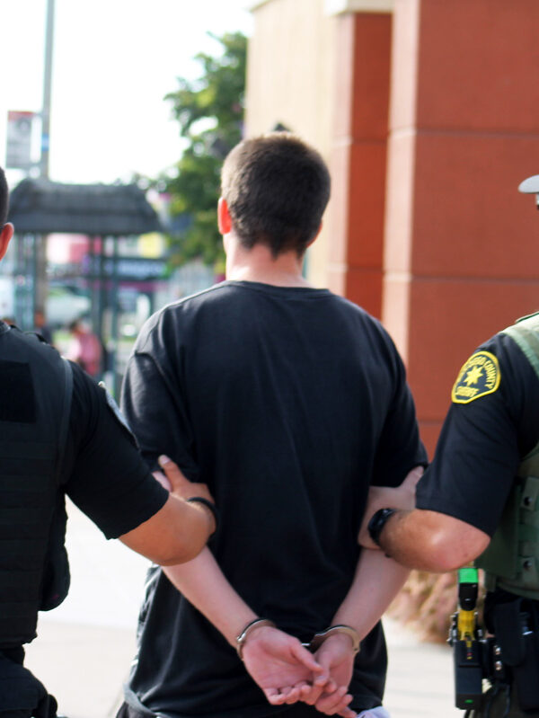 A male in handcuffs is being escorted away by a San Diego Police Department officer and a San Diego County Sherrif