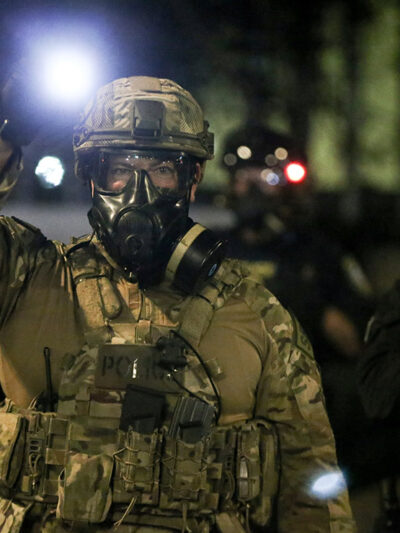 A group of militarized federal agents with an agent in the center shining a bright flashlight toward the viewer.