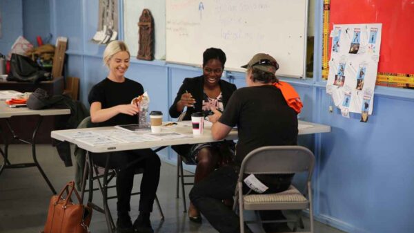 Three people gathered around a table appearing to be working on a project requring crafting.