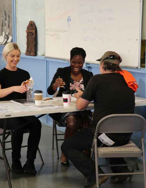 Three people gathered around a table appearing to be working on a project requring crafting.