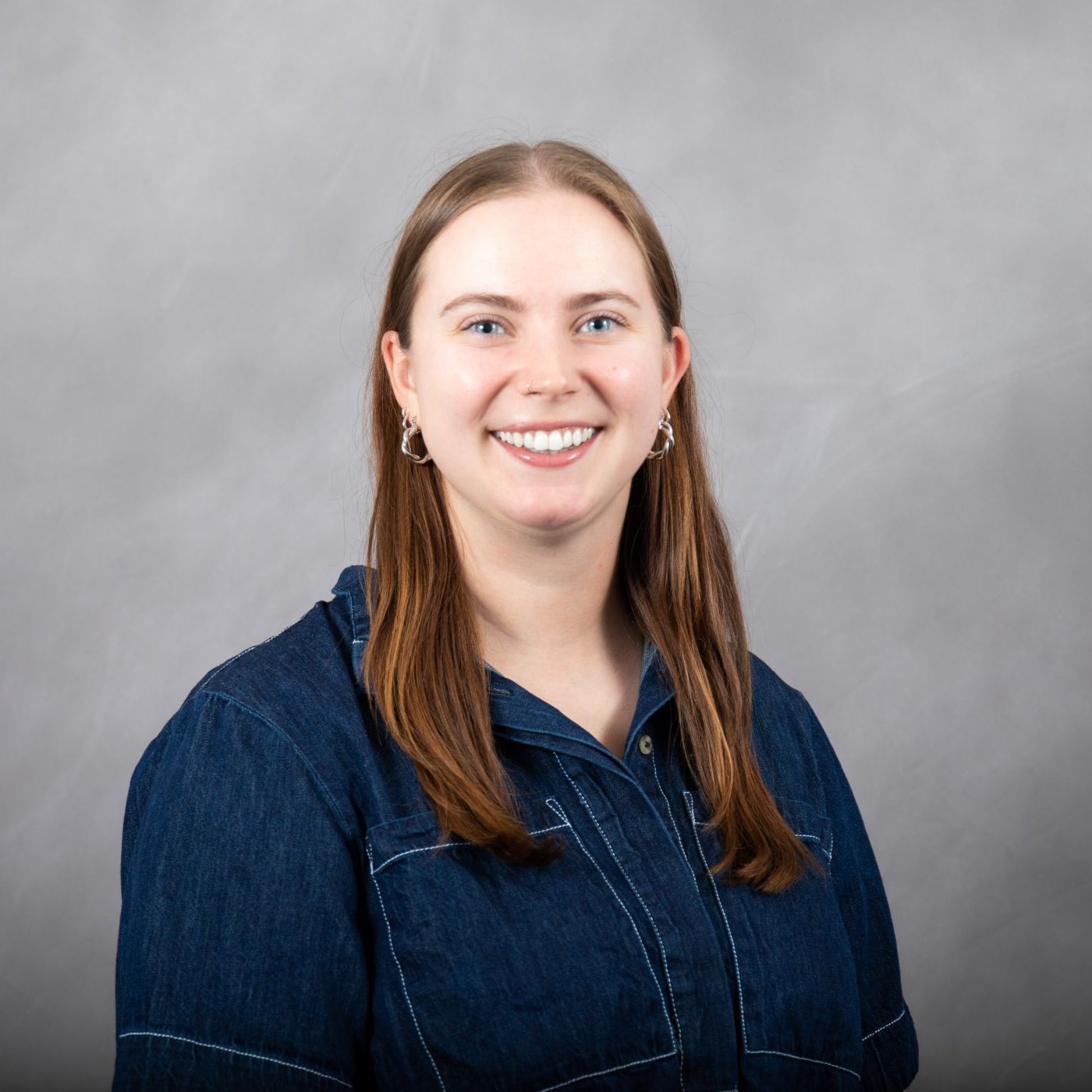 Photo of Maddie smiling at the camera. She is a white woman with brown hair wearing a blue shirt.