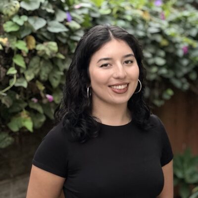 Photo of Kamilah smiling at the camera. She has dark curly hair and is wearing a black shirt.