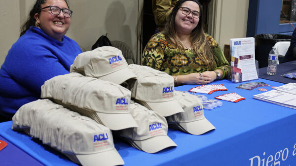 Daniela and Karolina at an event table giving out ACLU-SDIC hats and other resources.