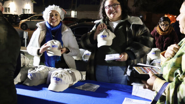 Crystal and Daniela holding ACLU-SDIC hats and smiling at the camera
