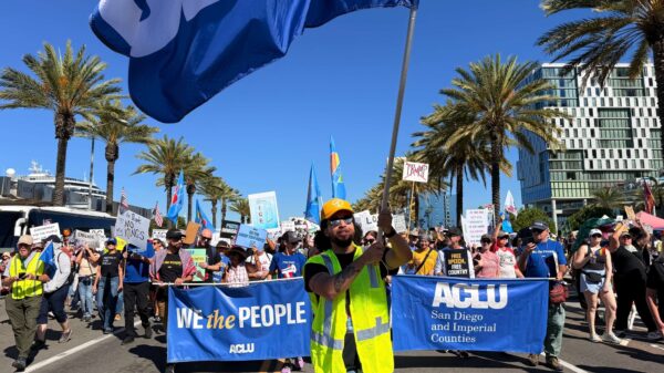 Jeff waves an ACLU flag in front of a group marching outdoors.