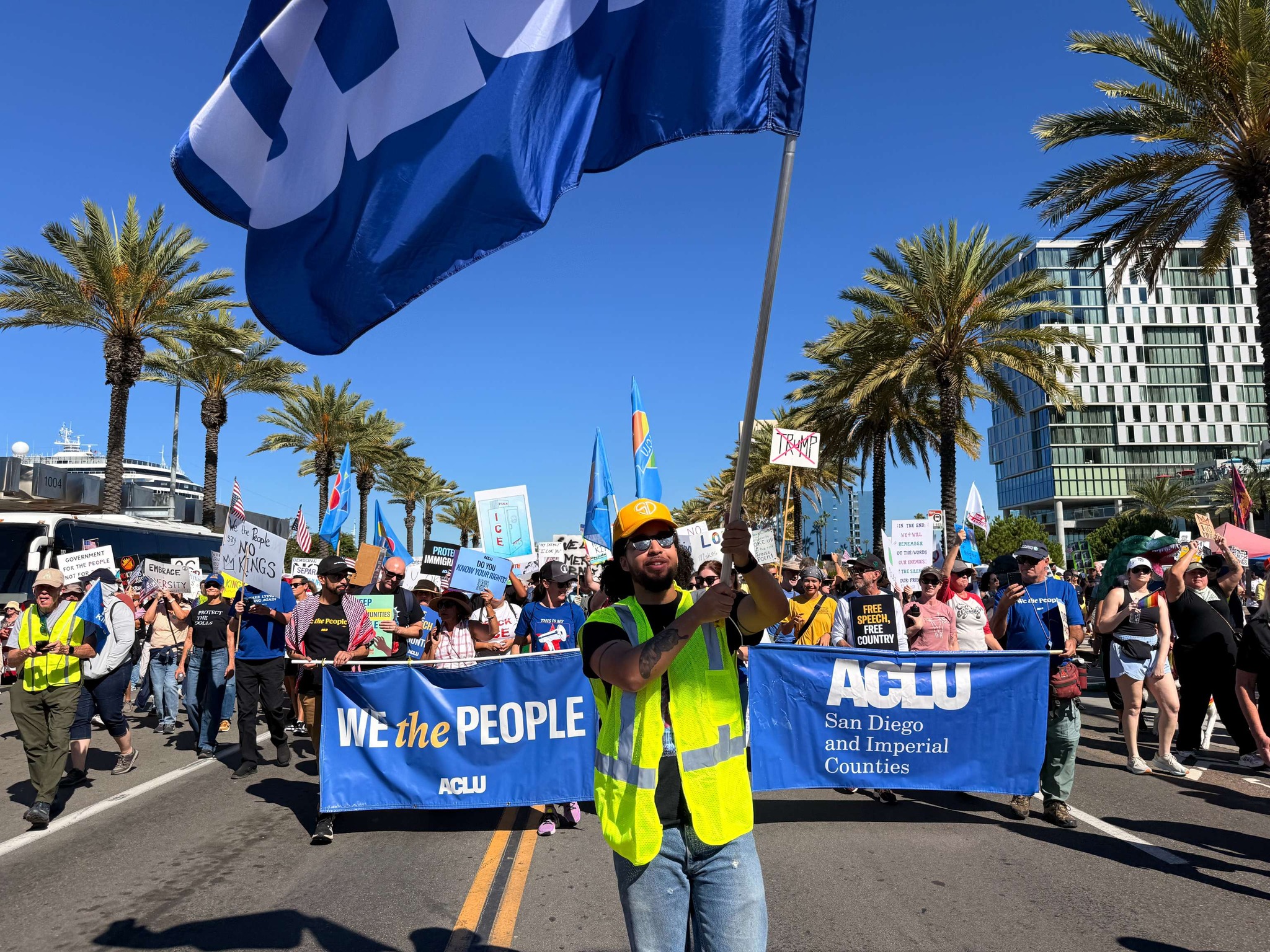 Jeff waves an ACLU flag in front of a group marching outdoors.