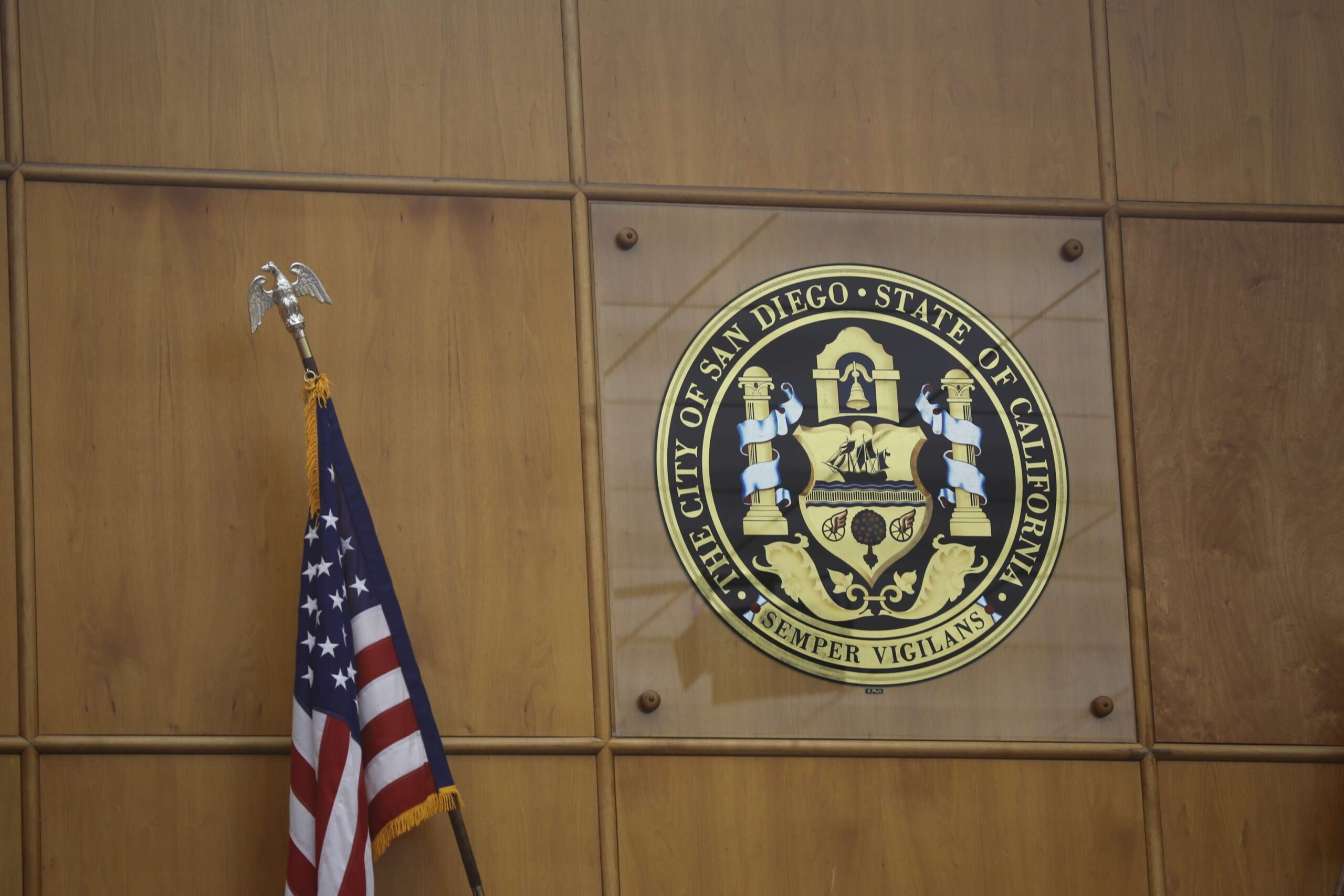 Photo of City of San Diego seal in the city council chambers. An American flag is in the left bottom corner.