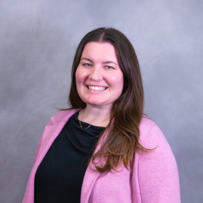Photo of Emilie smiling at camera in front of a gray backdrop.