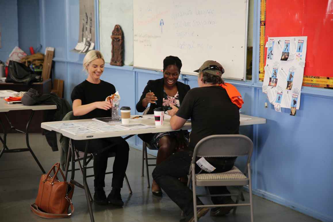 Three people gathered around a table appearing to be working on a project requring crafting.